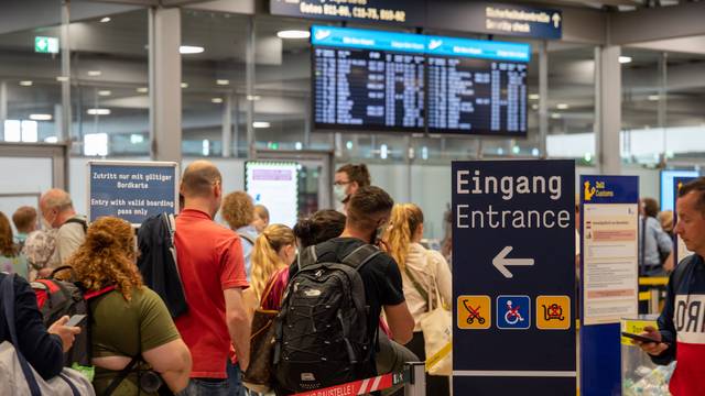 Am Flughafen Köln/Bonn warten Reisende im Sommer 2022 an der Sicherheitskontrolle. Es haben sich extrem lange Schlangen gebildet, im Hintergrund ist ein Fluganzeiger zu sehen. (Archivbild)