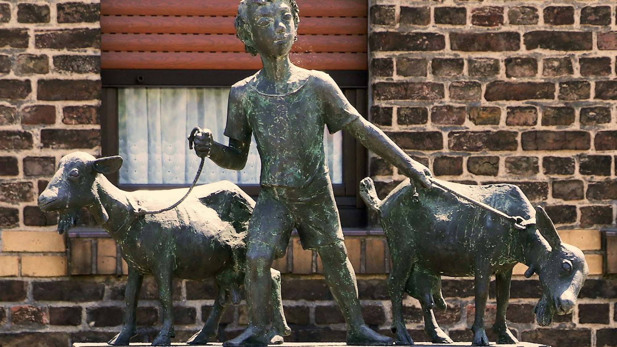 Eine Skulptur aus Bronze zeigt einen Jungen mit zwei Ziegen.