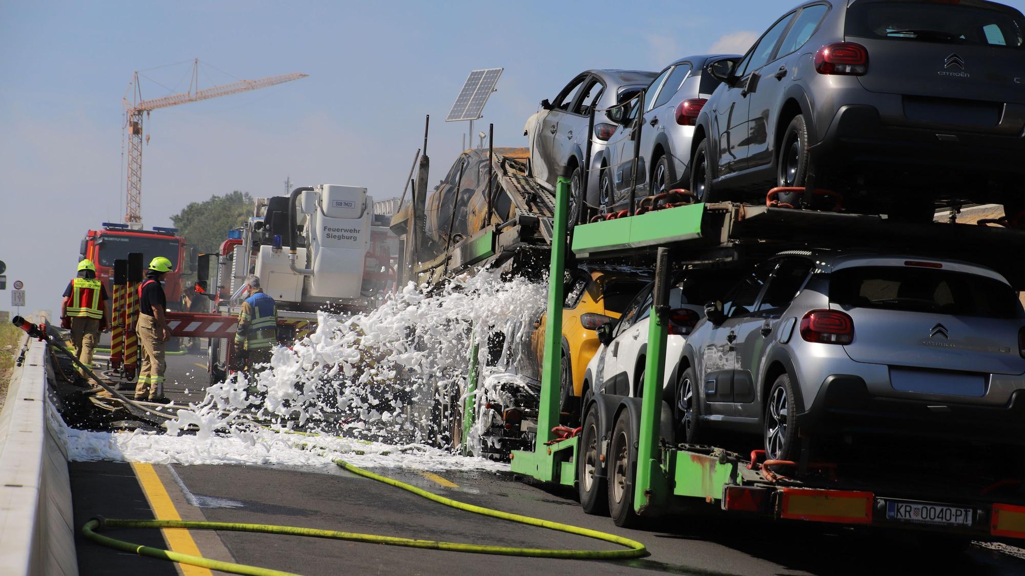 Feuerwehrleute sprühen Löschschaum auf einen brennenden Autotransporter.