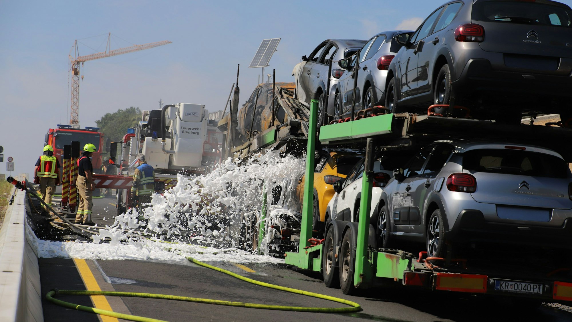 Feuerwehrleute sprühen Löschschaum auf einen brennenden Autotransporter.