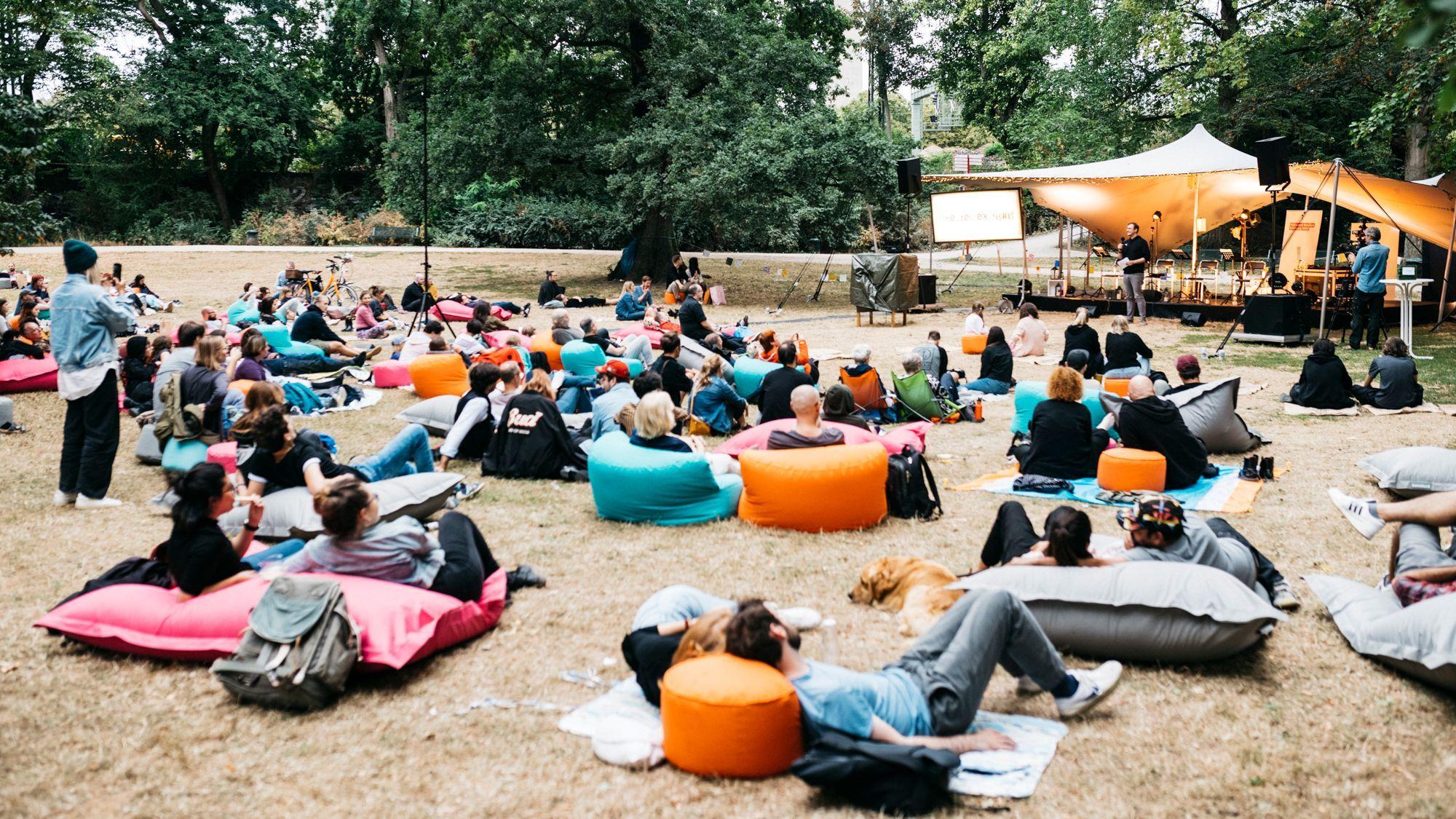 Viele Menschen liegen auf Sitzsäcken im Stadtgarten und schauen zu einer Bühne.