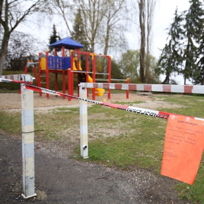 Ein Spielplatz ist mit rot-weißem Flatterband abgesperrt. Daran hängt ein roter Zettel.