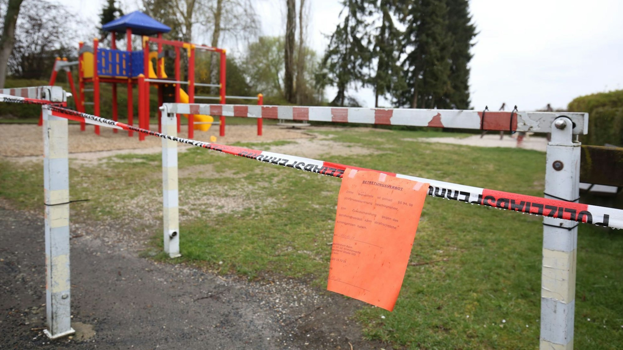Ein Spielplatz ist mit rot-weißem Flatterband abgesperrt. Daran hängt ein roter Zettel.