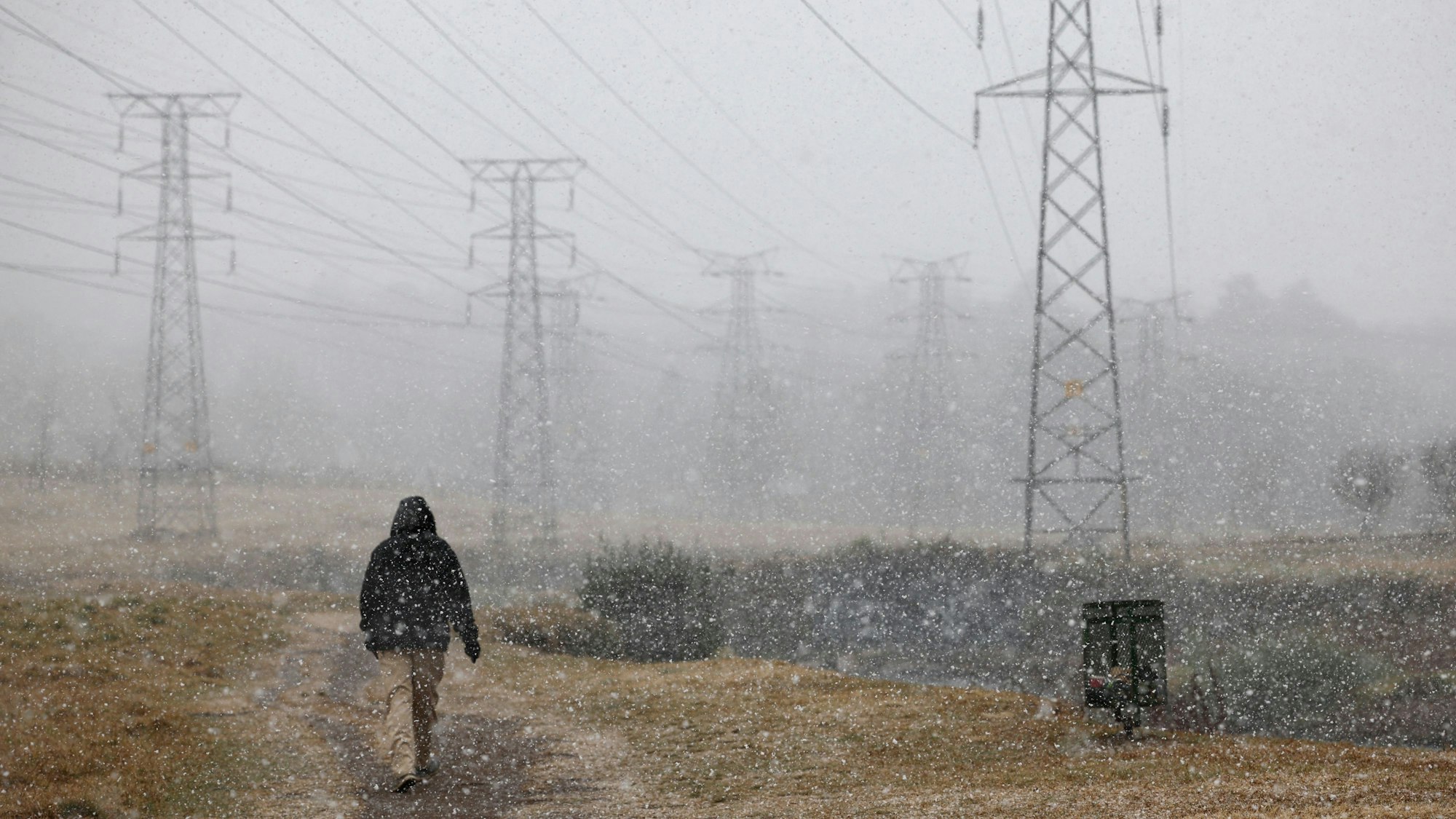 A man walks on a pathway as snow falls in Delta Park, Johannesburg, on July 10, 2023. (Photo by Wikus de Wet / AFP)