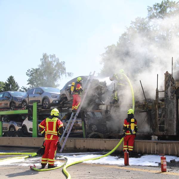 Feuerwehrleute löschen einen brennenden Autotransporter.