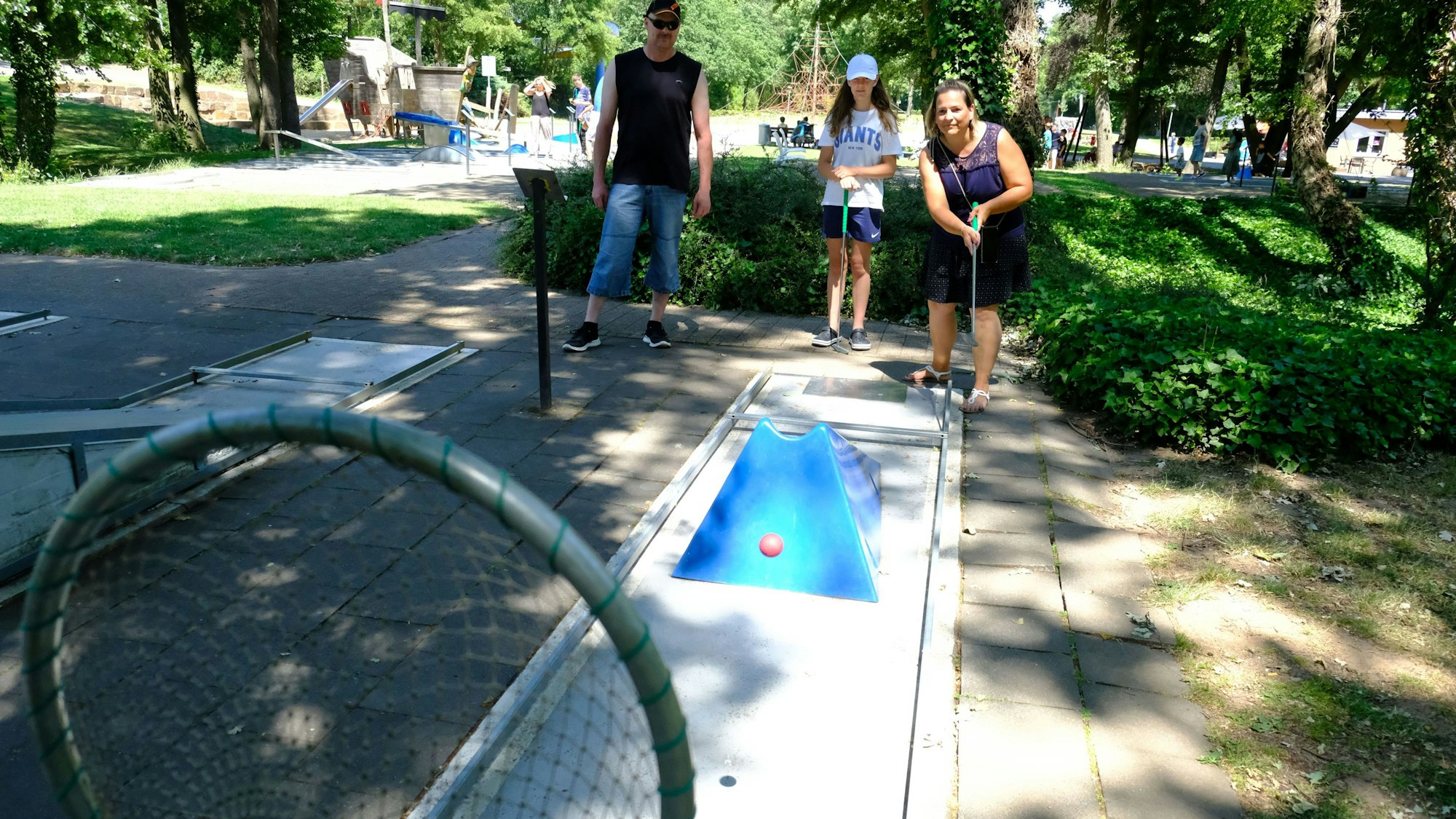 Eine dreiköpfige Familie spielt Minigolf.