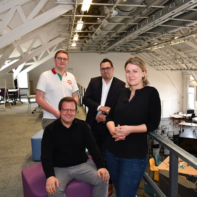 Drei Männer und eine Frau auf der Empore eines Großraumbüros.