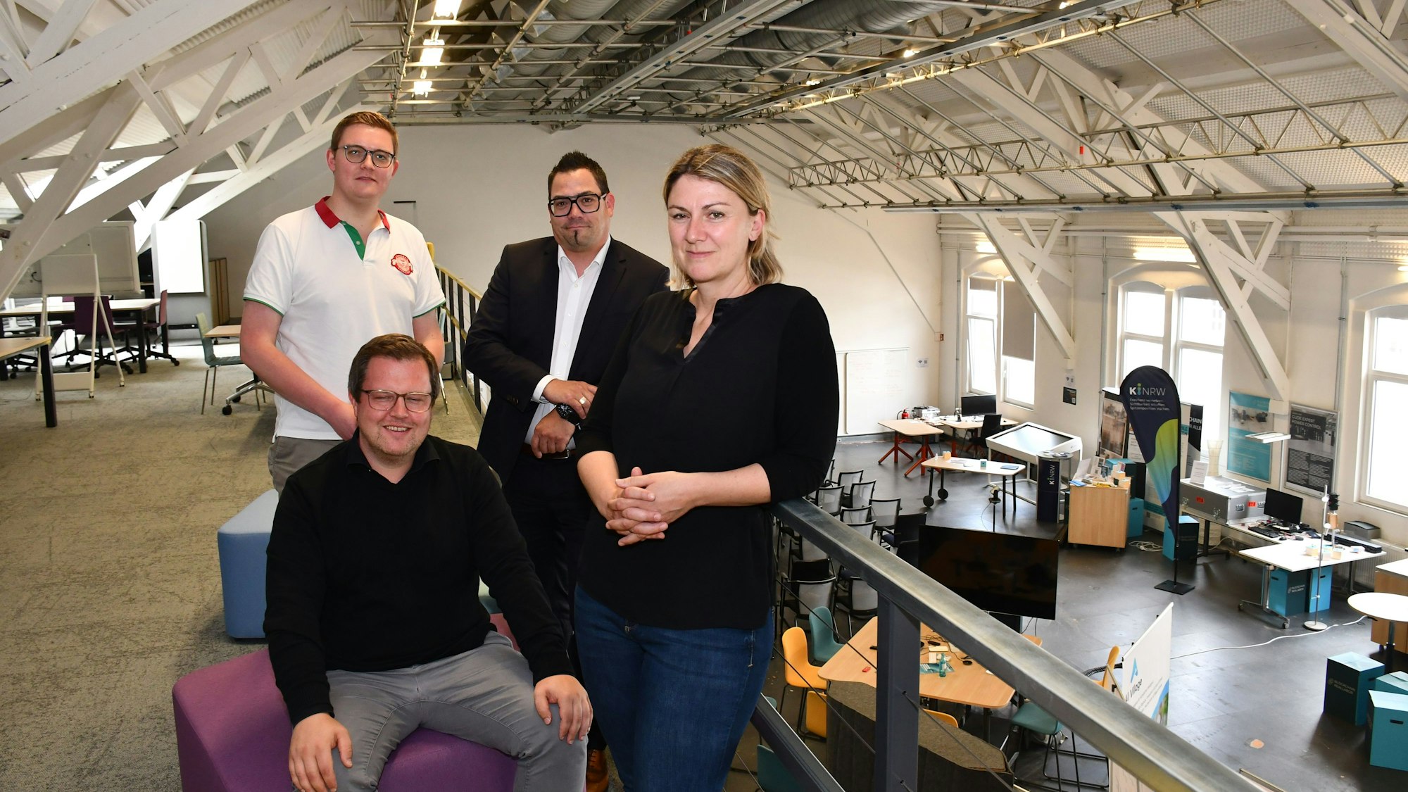 Drei Männer und eine Frau auf der Empore eines Großraumbüros.