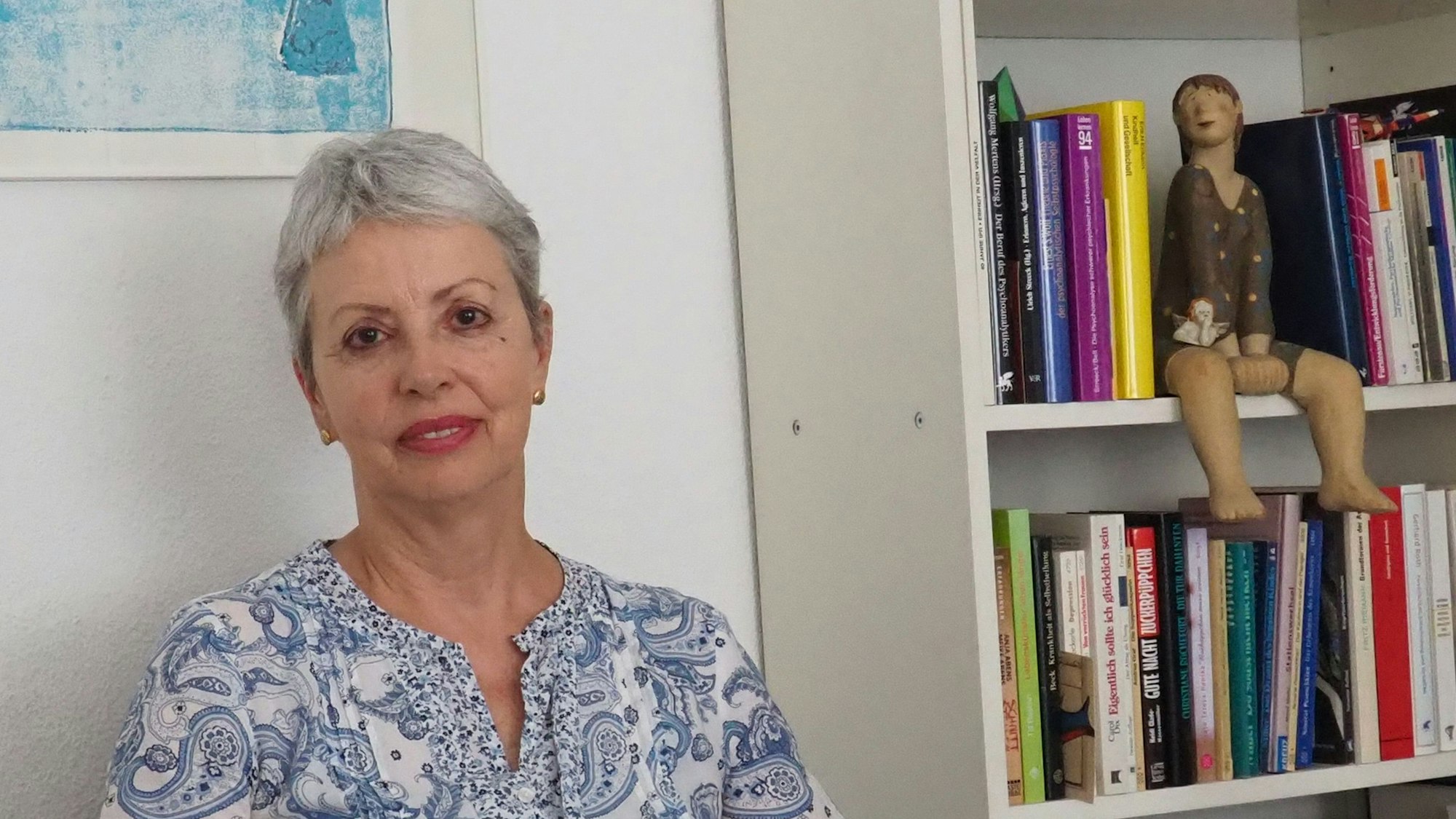 Eine Frau sitzt neben einem Bücherregal.