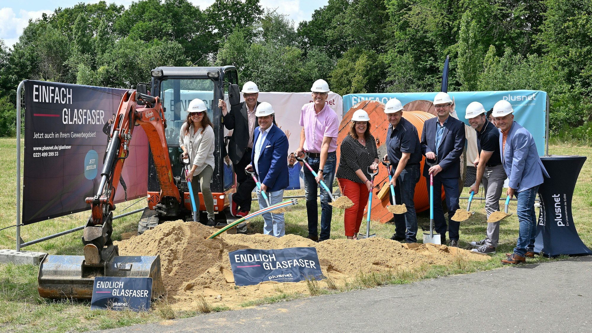 Mehrere Personen stehen vor einem Werbebanner und halten symbolische Spaten in der Hand.