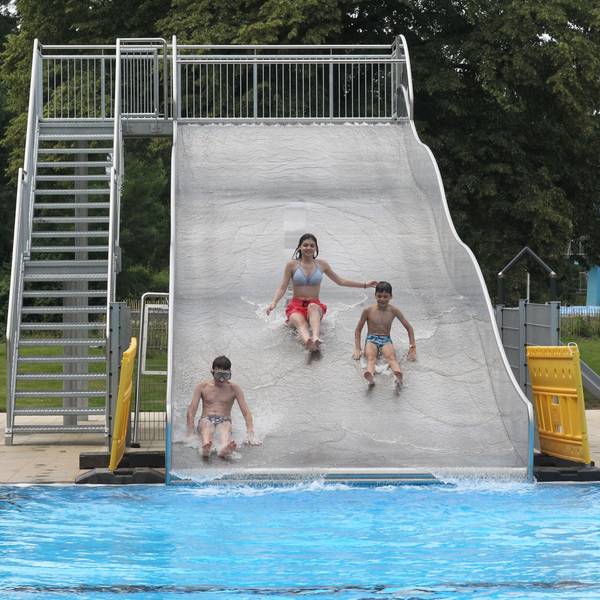 Drei Kinder rutschen eine Wasserrutsche in einem Schwimmbad herunter.