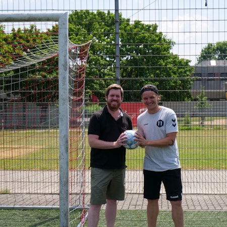 Zwei Männer stehen vor einem Fußballtor und halten einen Fußball in den Händen.