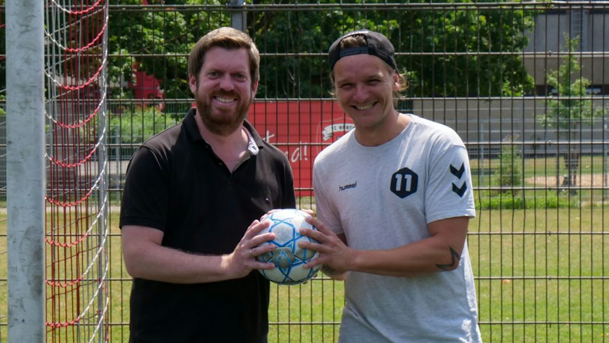 Zwei Männer stehen vor einem Fußballtor und halten einen Fußball in den Händen.