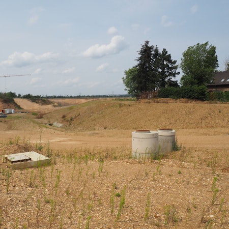 In einer flachen, sandigen Mulde sind Baumaschinen zu sehen.