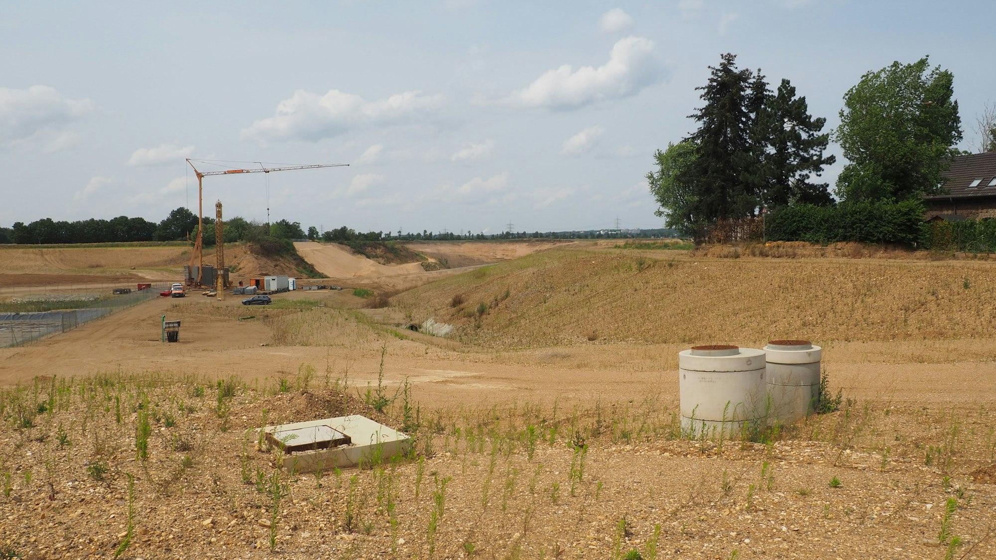 In einer flachen, sandigen Mulde sind Baumaschinen zu sehen.