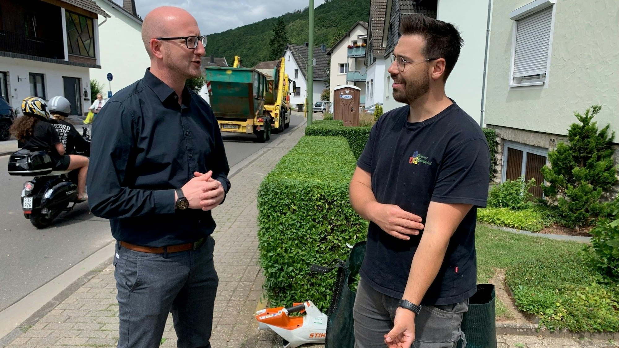 Alexander Geschwind arbeitet in einem Vorgarten in Gemünd-Malsbenden. Er berichtet Bürgermeister Ingo Pfennings vom Stand des Wiederaufbaus im Gärtnerei-Betrieb seiner Familie.
