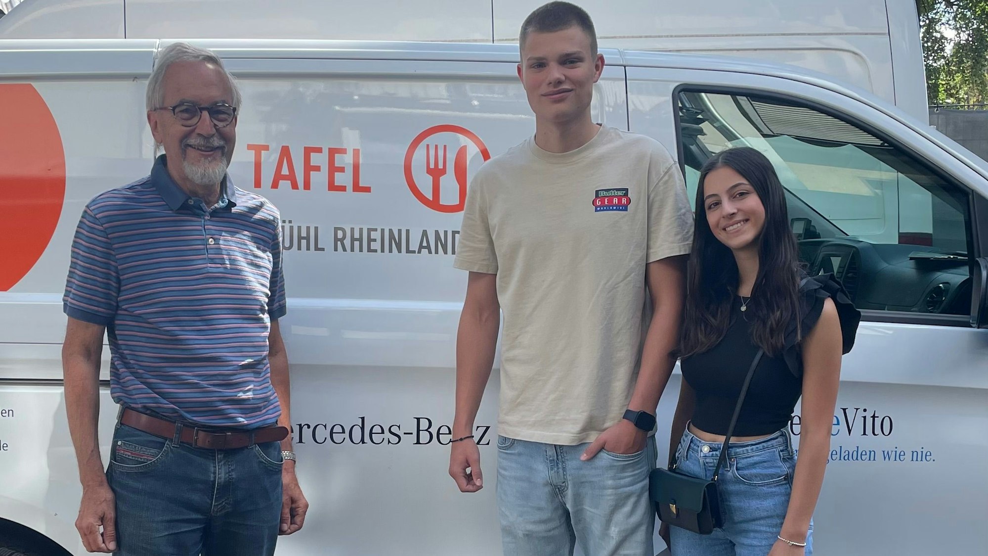 Das Bild zeigt einen der Verantwortlichen der Brühler Tafel sowie eine Abiturientin und einen Abiturienten vor einem Wagen der Tafel.