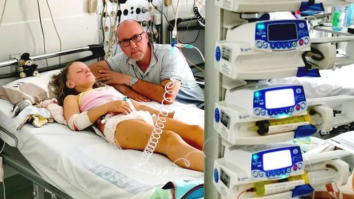 Die elfjährige Lara liegt mit geschlossenen Augen im Krankenbett, Dirk Rohde sitzt neben ihr.