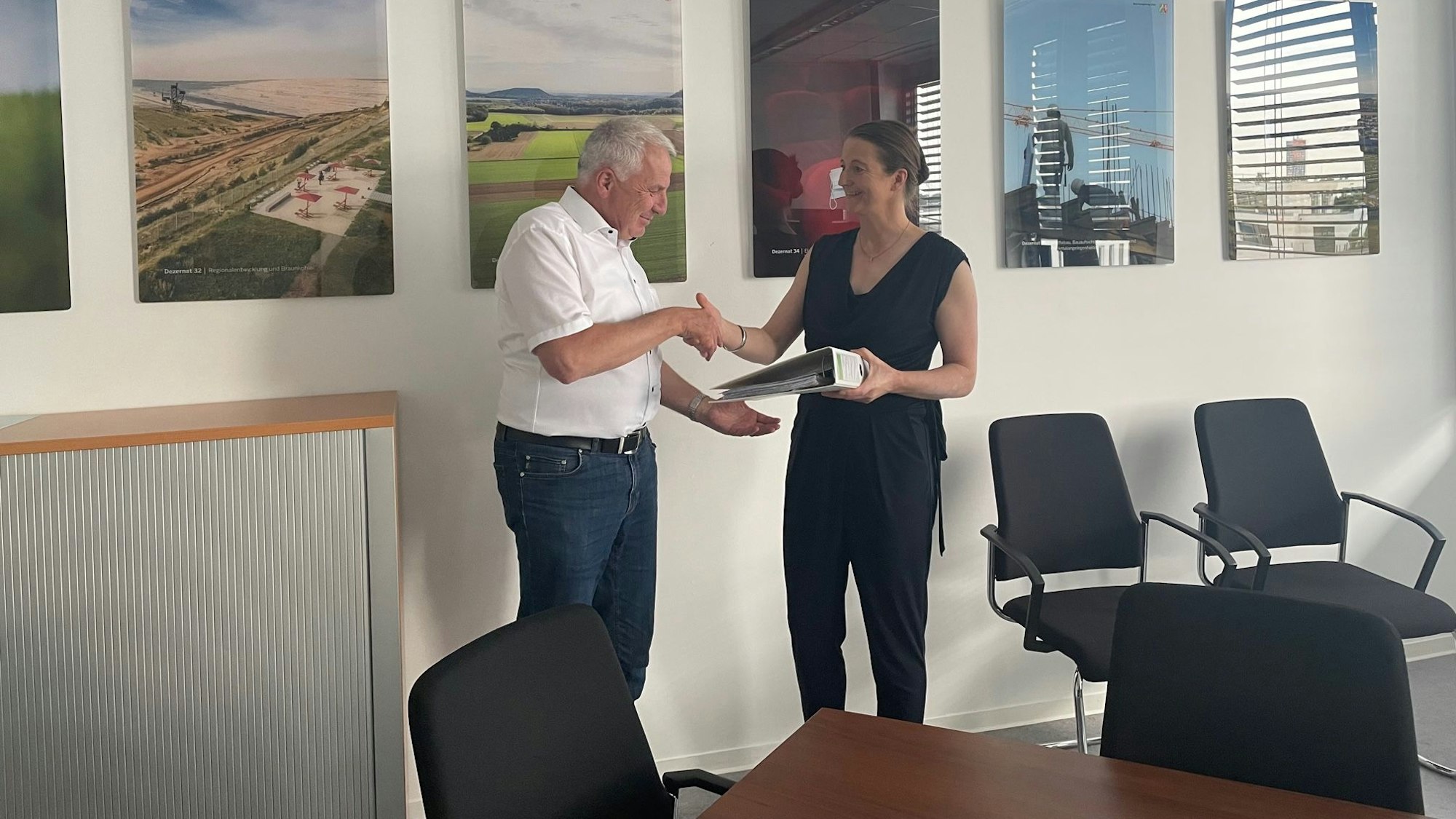 Annika Effertz gibt Rainer Deppe den Ordner mit der Unterschriftenliste.