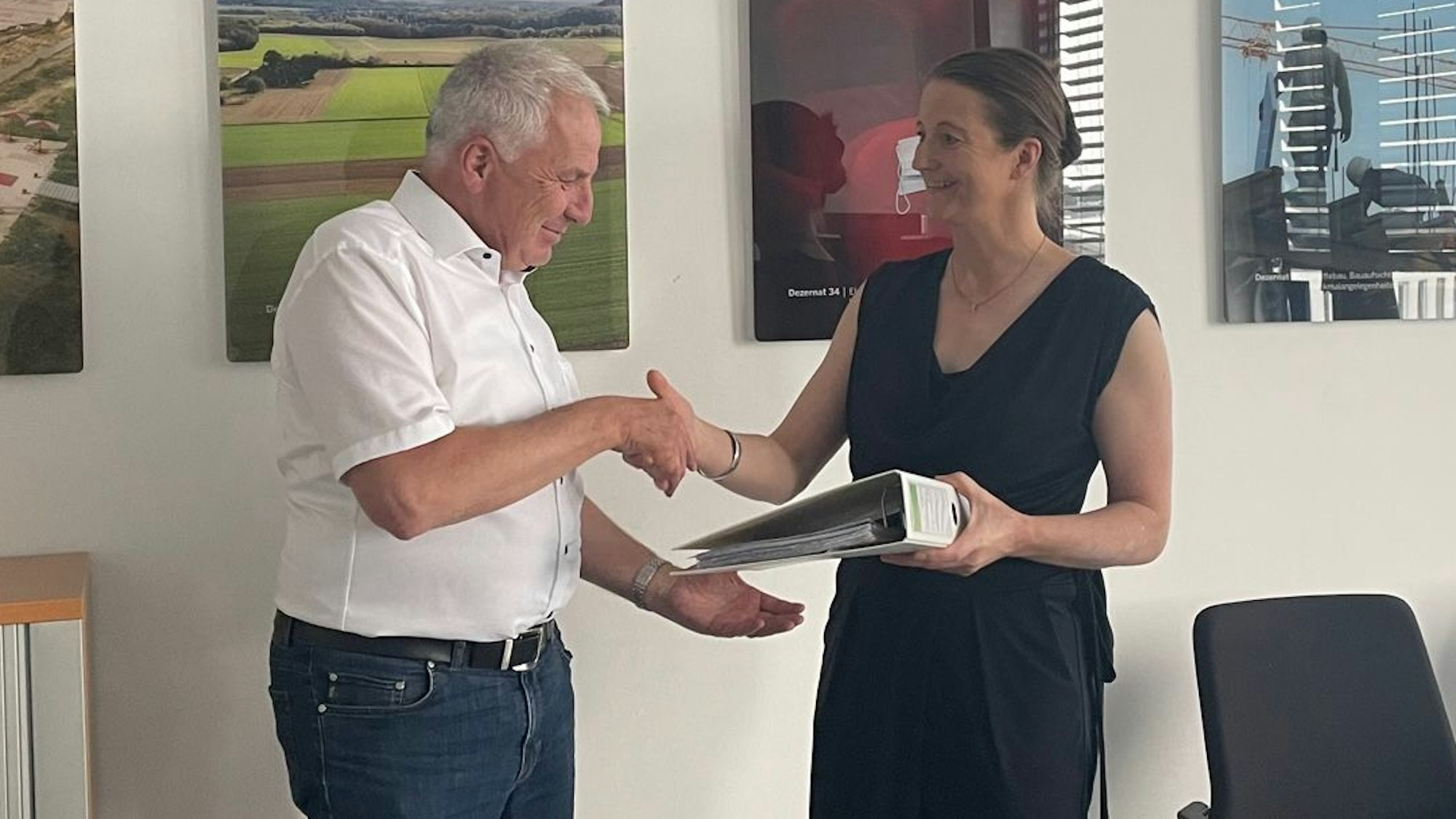 Auf dem Foto sind die Grünen-Politikerin Annika Effertz und Rainer Deppe vom Regionalrat Köln zu sehen. Sie überreicht ihm einen Ordner mit Unterschriften gegen ein geplantes Gewerbegebiet in Kerpen.