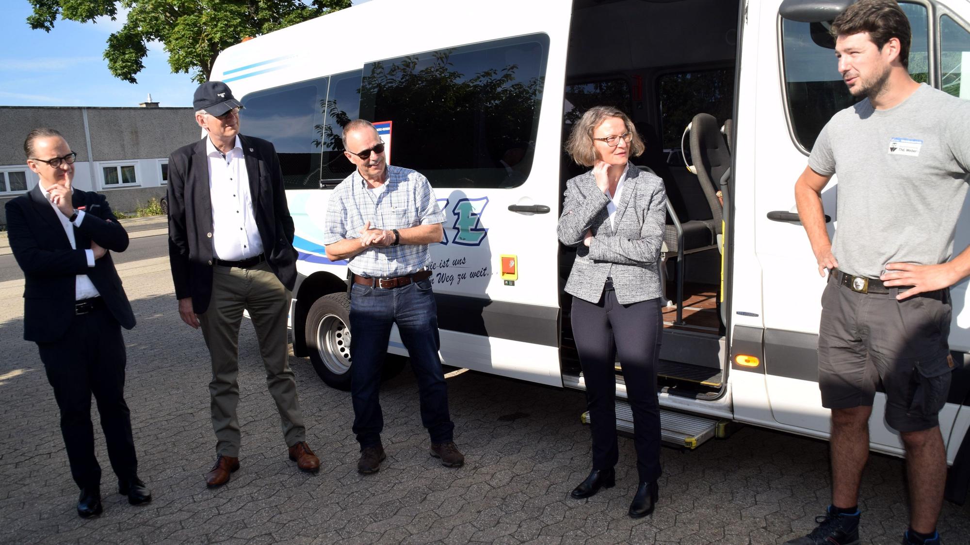 Ministerin Ina Scharrenbach und vier Männer stehen vor einem Kleinbus und unterhalten sich.