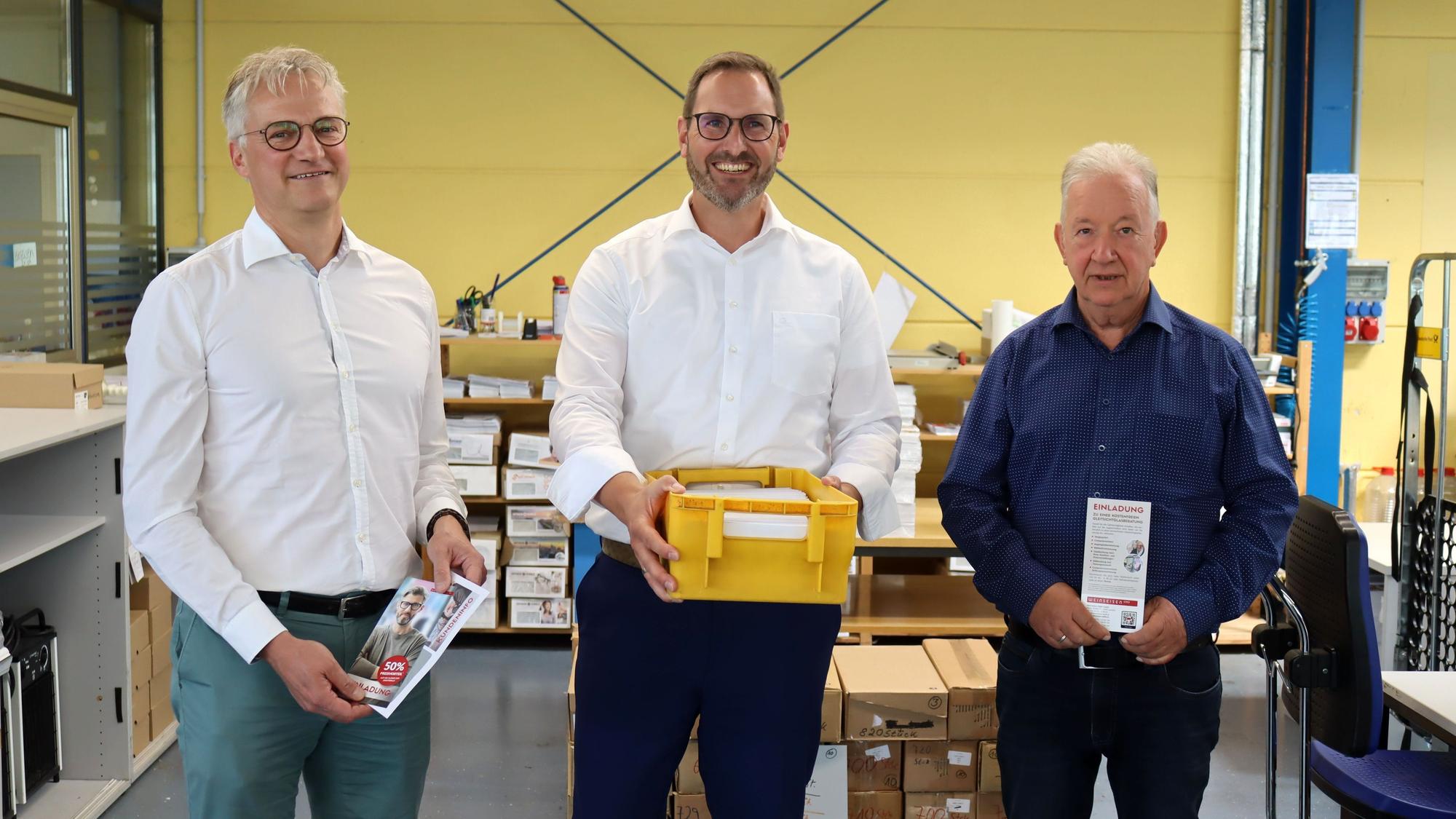Die drei Geschäftsführer der Nordeifel-Werkstätten stehen in einer der Werkhallen in Kuchenheim nebeneinander.