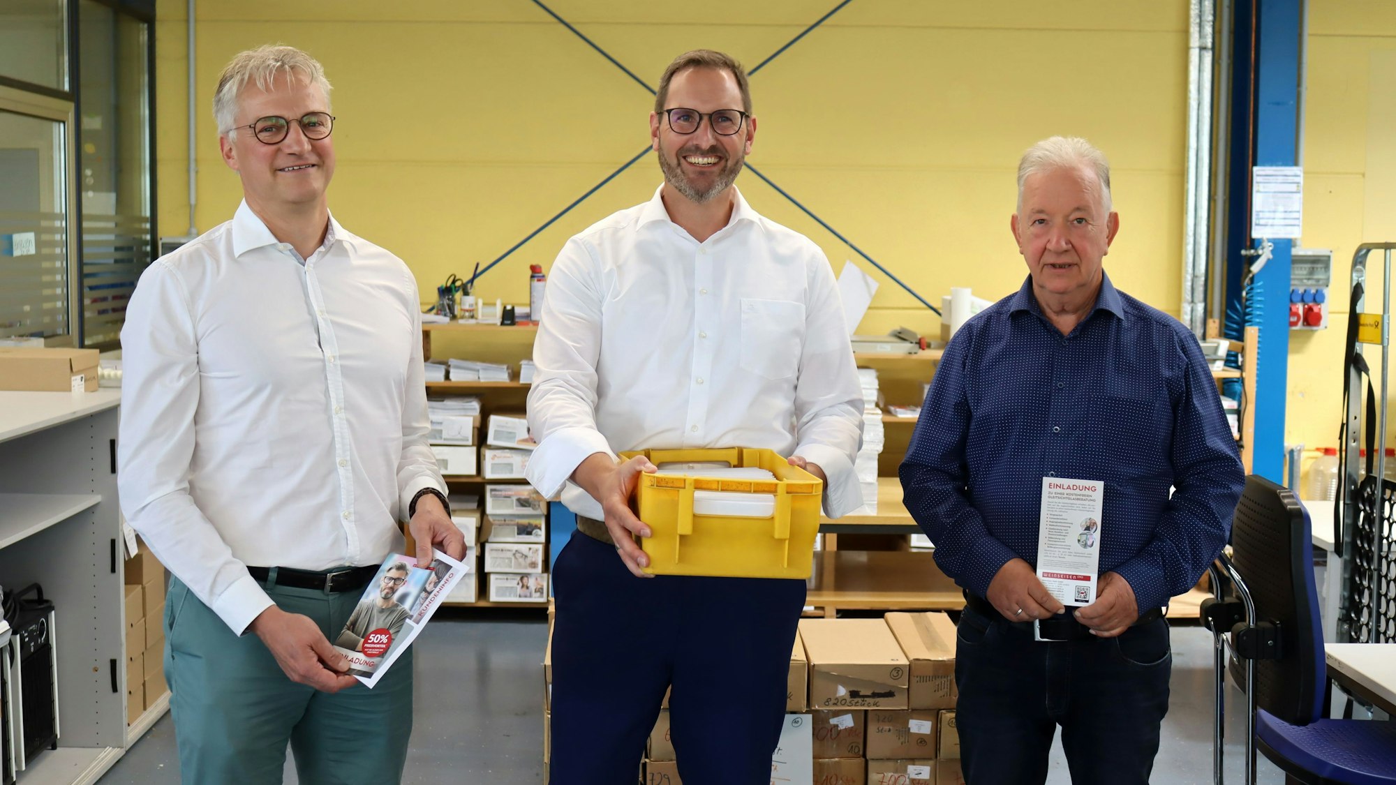 Die drei Geschäftsführer der Nordeifel-Werkstätten stehen in einer der Werkhallen in Kuchenheim nebeneinander.