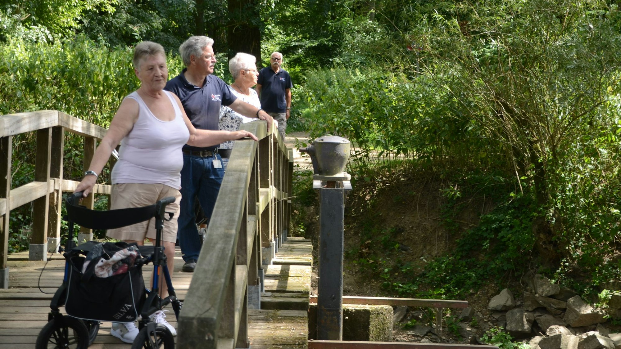 Eine Frau mit Rollator steht auf einer Holzbrücke