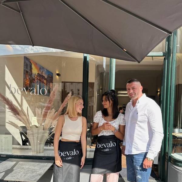 Zwei Frauen und ein Mann stehen vor einem Café.