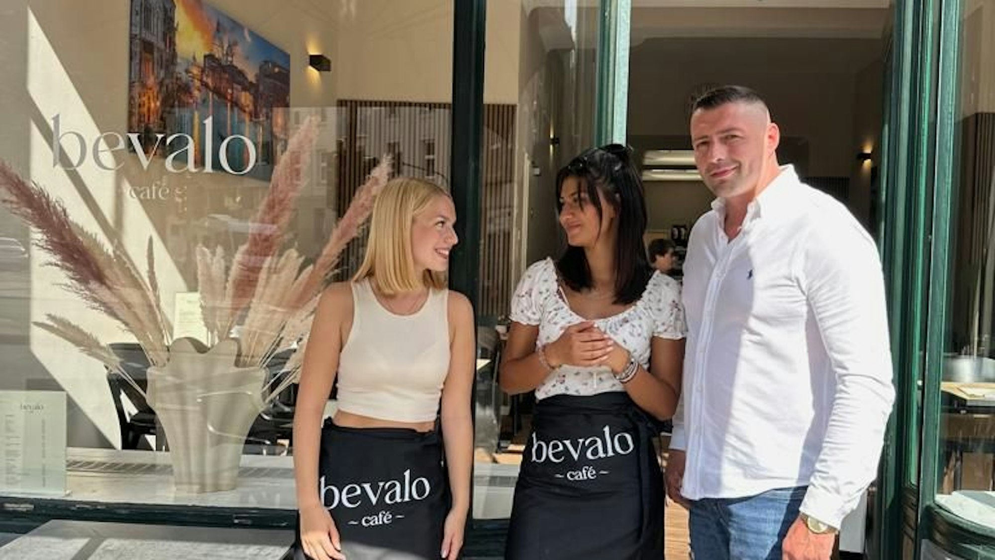 Zwei Frauen und ein Mann stehen vor einem Café.