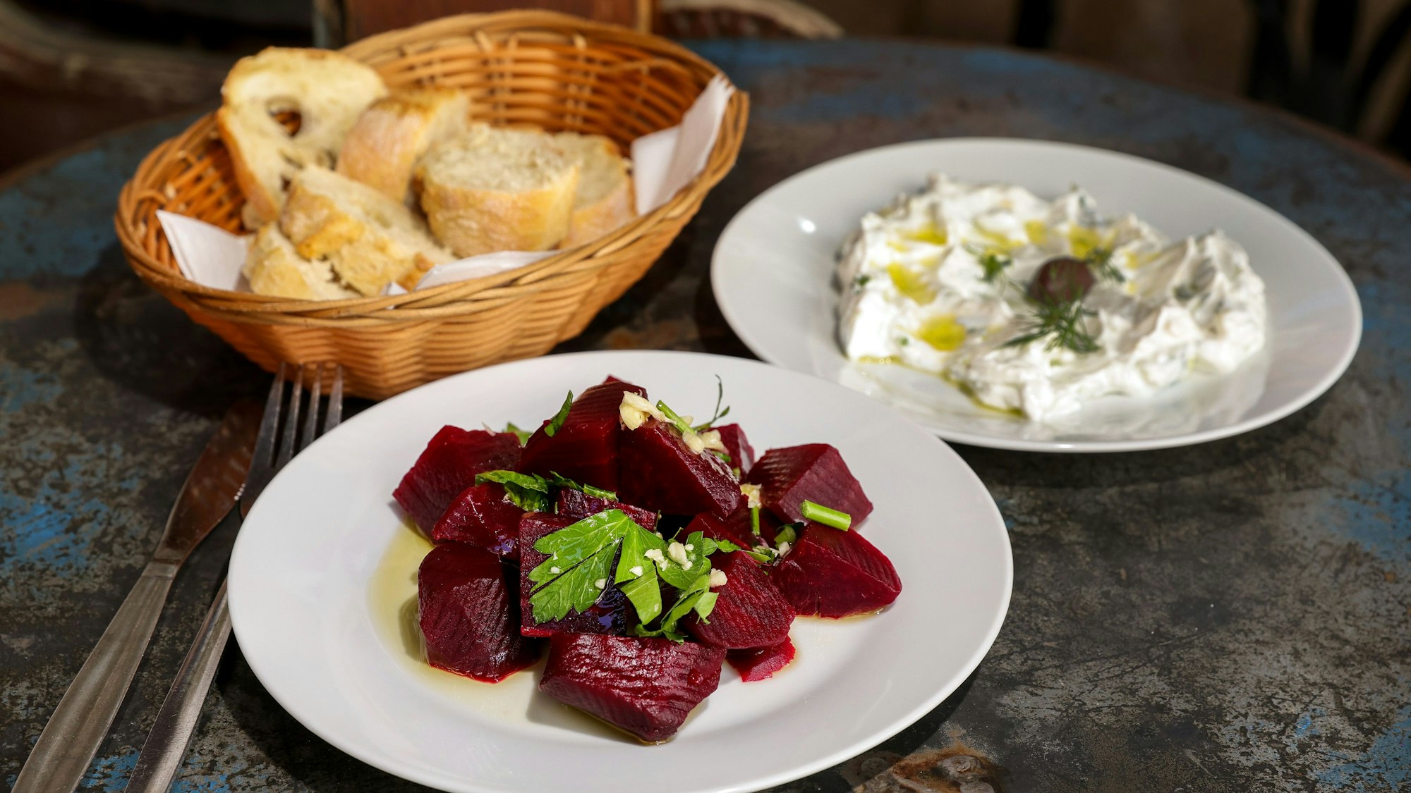 Rote-Bete-Salat Tsatsiki und Brot im Korb stehen auf einem Tisch.