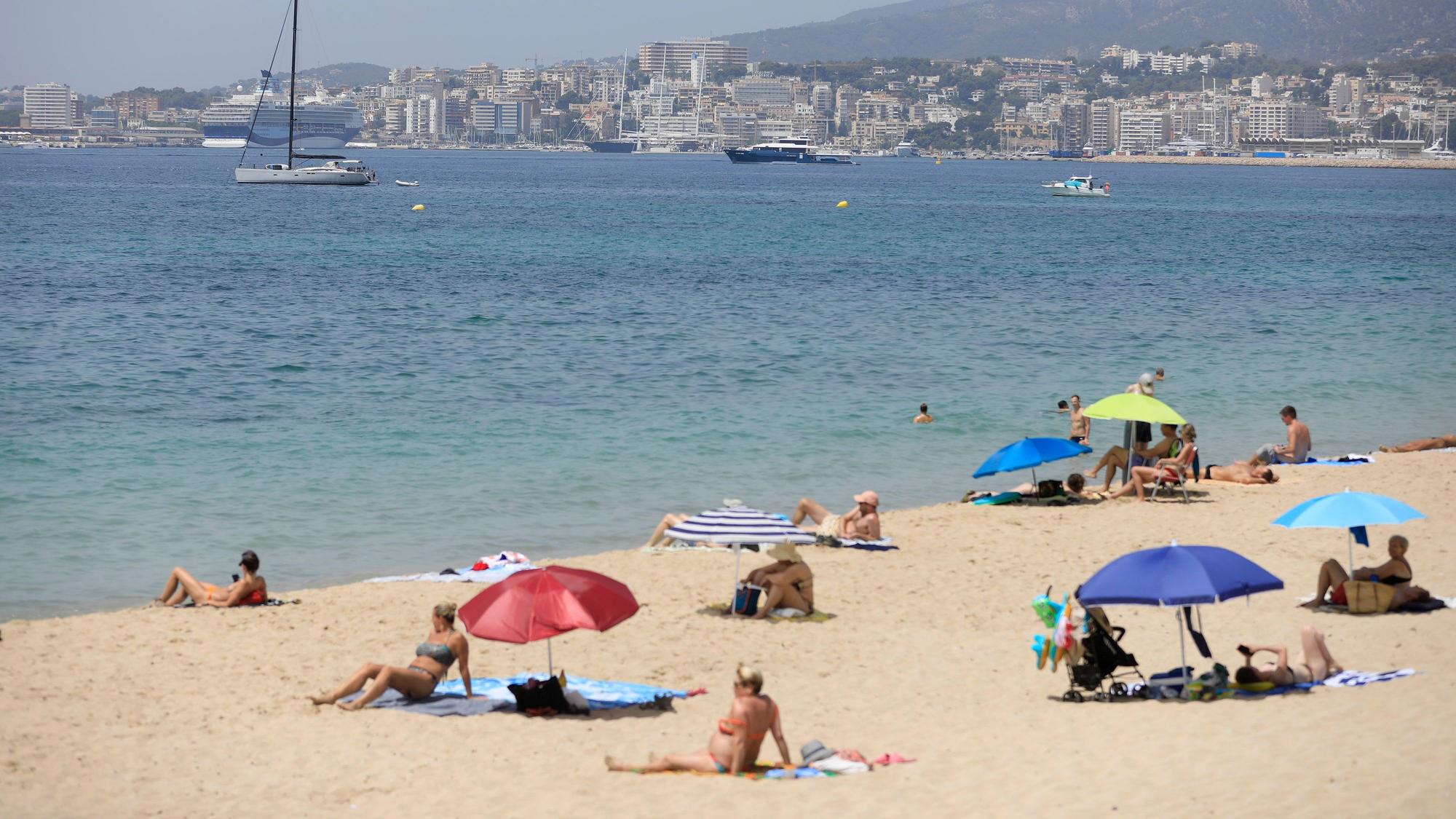 08.07.2023, Spanien, Palma: Menschen sonnen sich und benutzen Sonnenschirme am Strand Can Pere Antoni in Palma während einer Hitzewelle