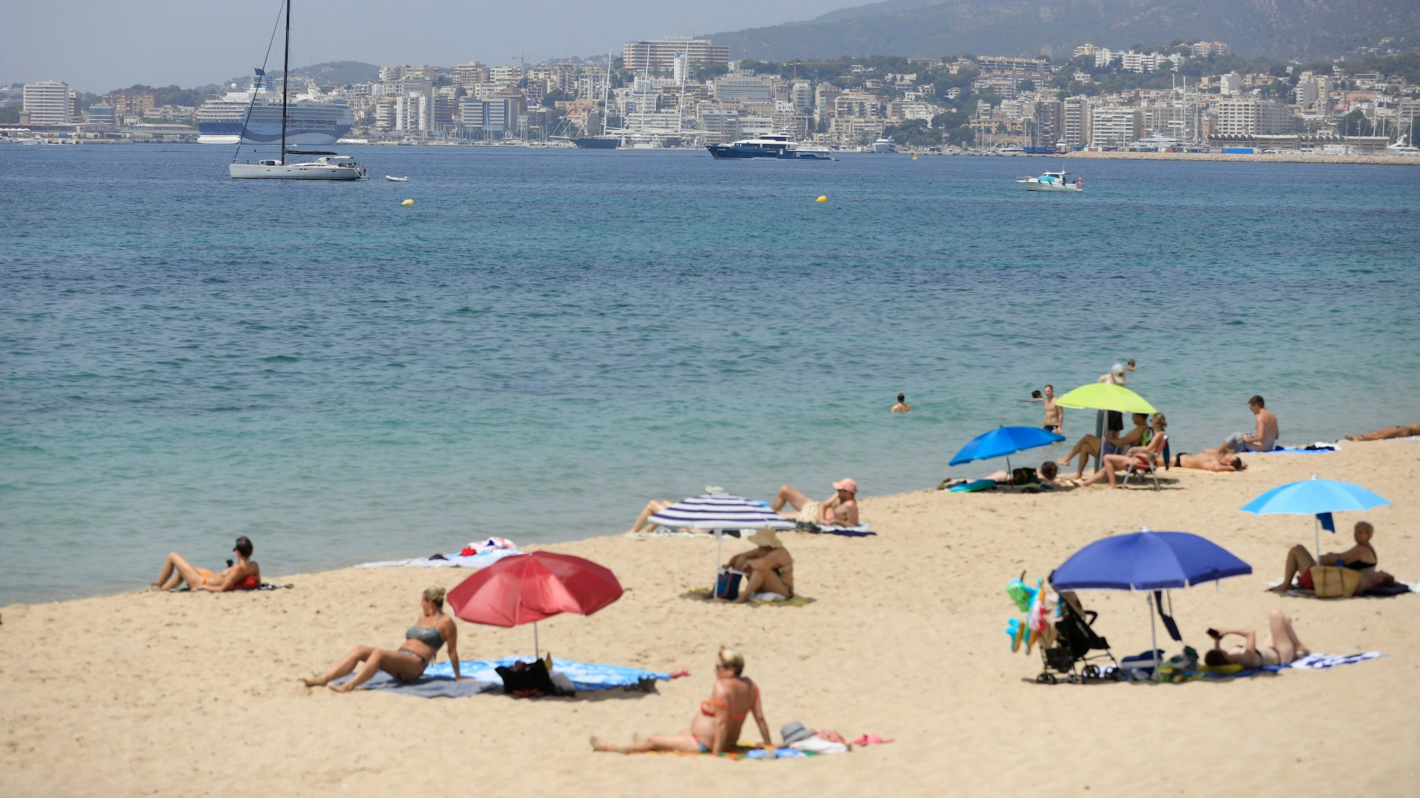 08.07.2023, Spanien, Palma: Menschen sonnen sich und benutzen Sonnenschirme am Strand Can Pere Antoni in Palma während einer Hitzewelle