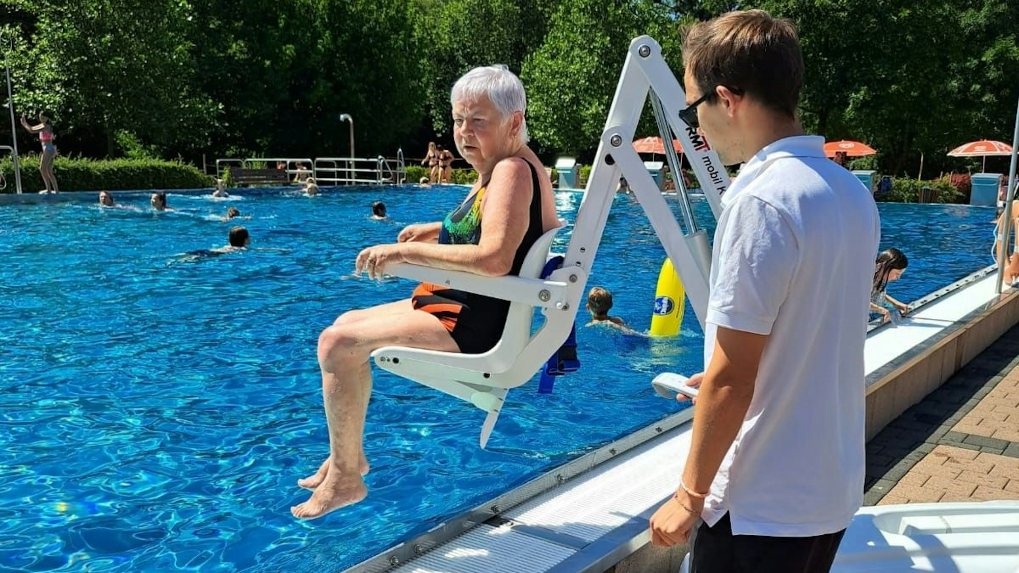 Ein ältere Dame wird mit einem weißen Sitz ins Becken gehoben. Im Bedburger Freibad gibt es jetzt einen neuen Lift, der den Einstieg ins Becken erleichtert.