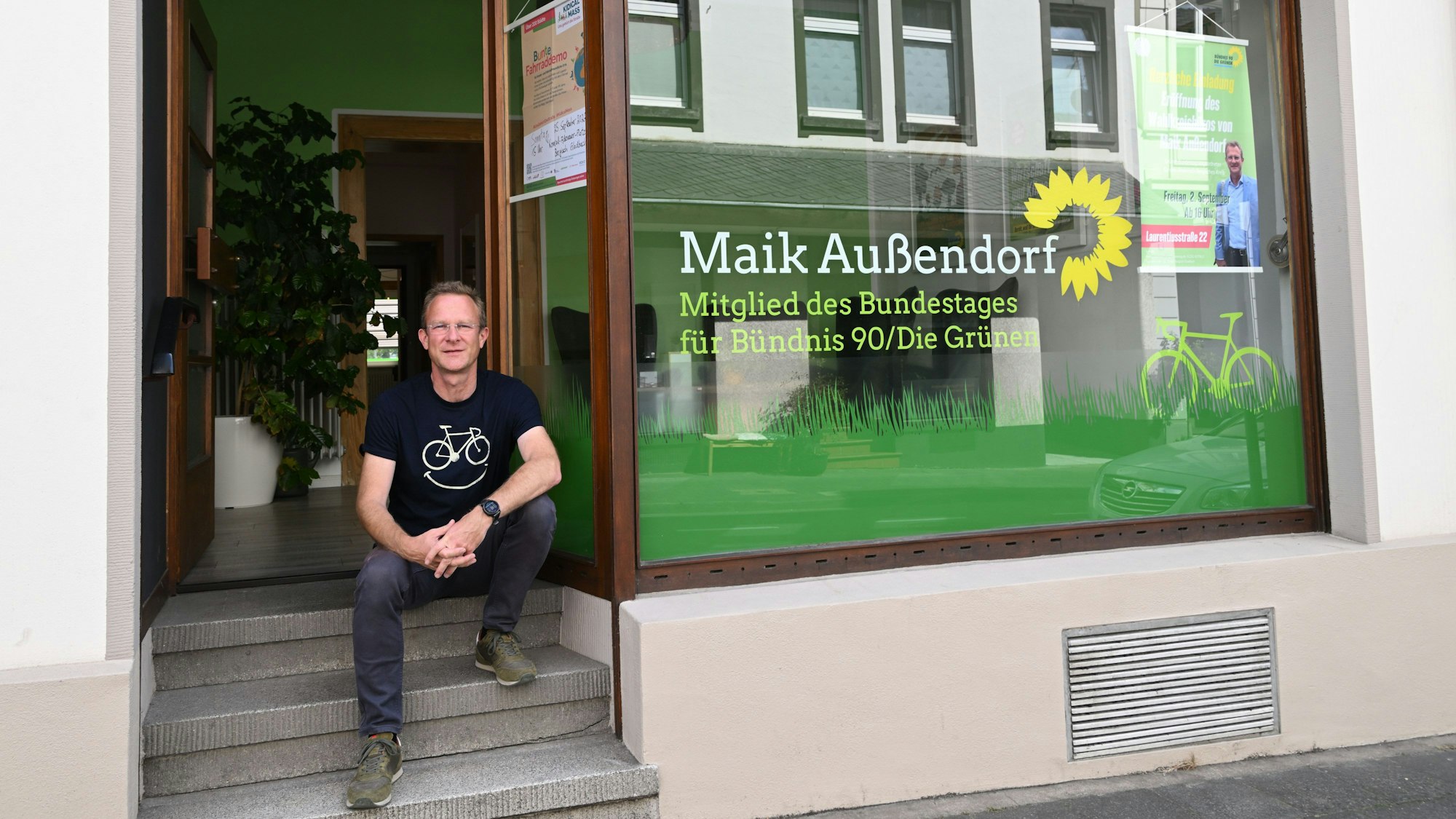 Maik Außendorf sitzt vor Grünem Wahlkreisbüro.