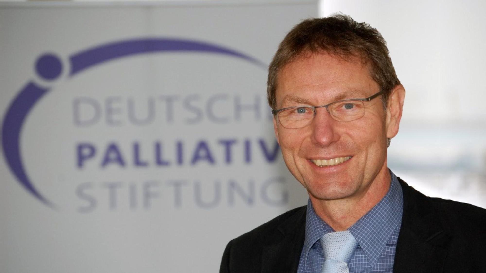 Porträtfoto von Thomas Sitte vor einem Banner der Deutschen PalliativStiftung