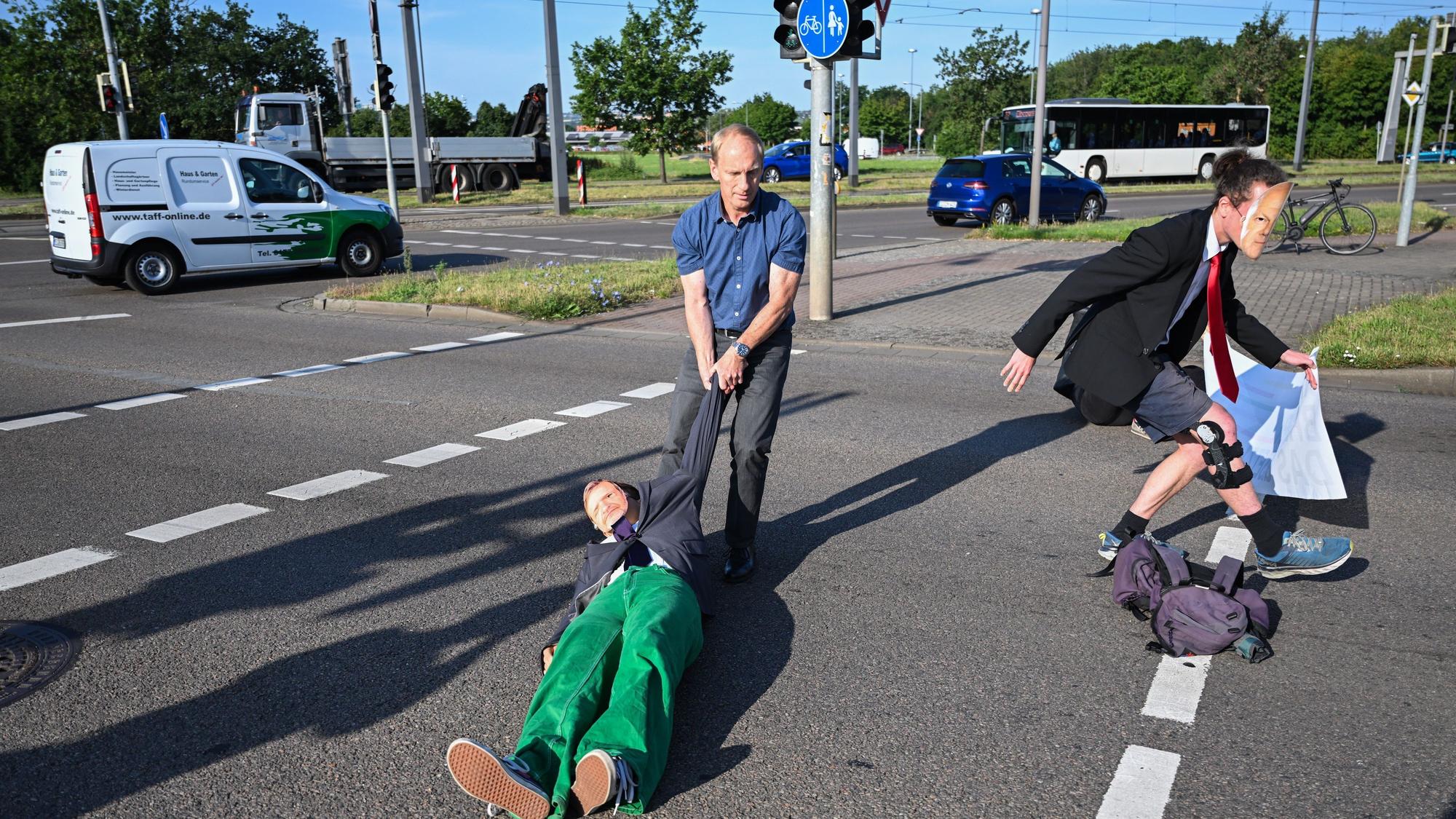 Ein Mitglied der Protestgruppe Letzte Generation wird bei einer Sitzblockade an der Autobahnabfahrt am Elbepark von einem Autofahrer (M) beiseite gezogen. Die Demonstranten tragen Masken mit den Portraits von Bundeswirtschaftsminister Habeck (l) und Bundeskanzler Scholz.