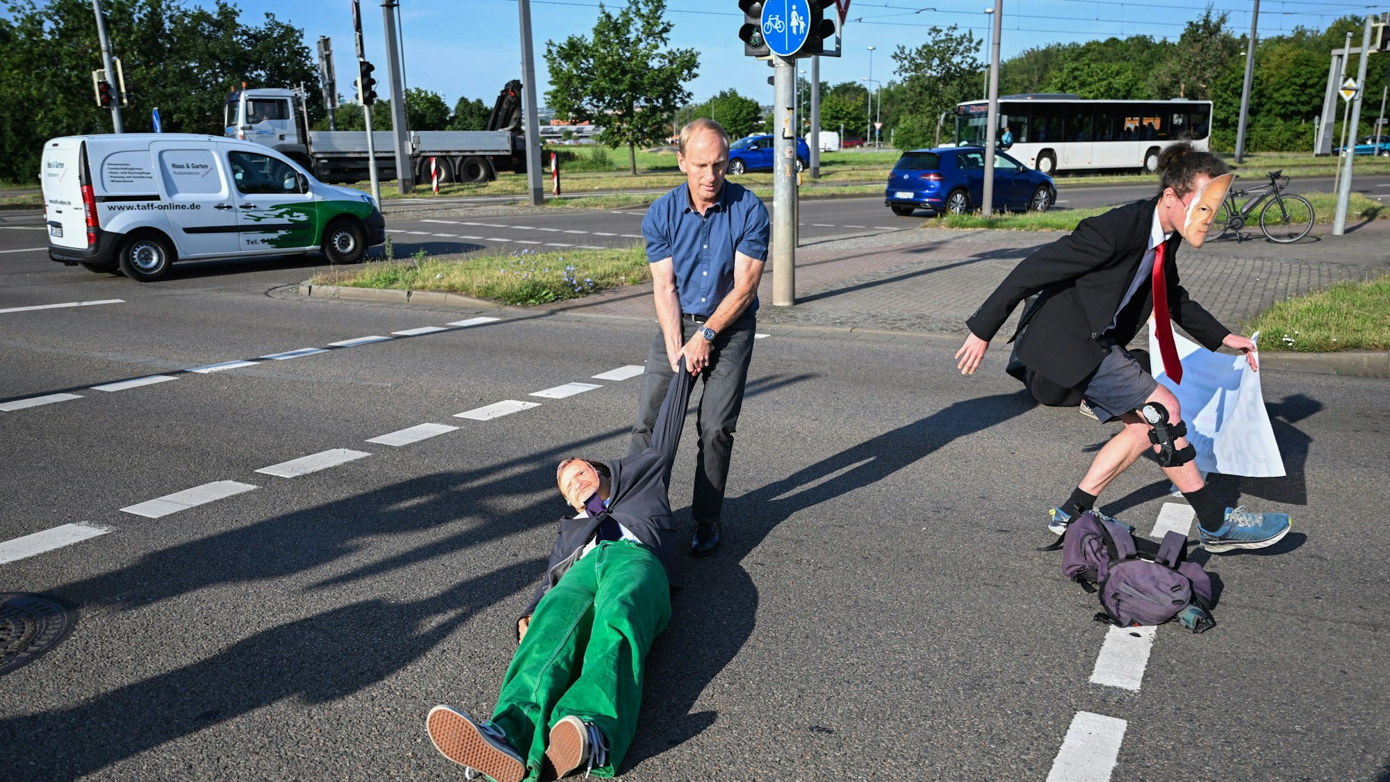 Ein Mitglied der Protestgruppe Letzte Generation wird bei einer Sitzblockade an der Autobahnabfahrt am Elbepark von einem Autofahrer (M) beiseite gezogen. Die Demonstranten tragen Masken mit den Portraits von Bundeswirtschaftsminister Habeck (l) und Bundeskanzler Scholz.