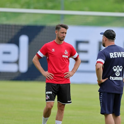 Mark Uth steht mit Steffen Baumgart auf dem Rasen und unterhält sich.