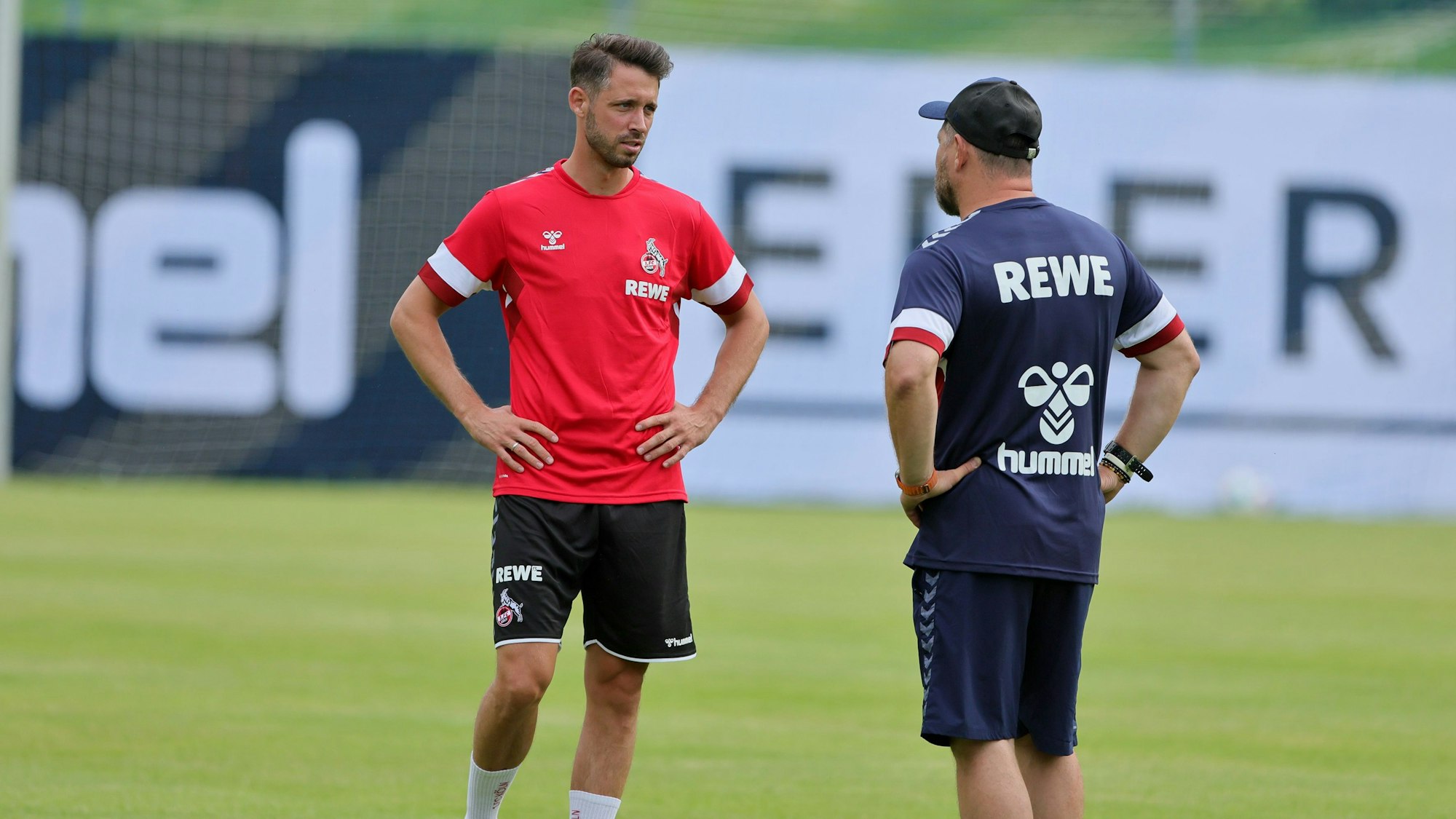 Mark Uth steht mit Steffen Baumgart auf dem Rasen und unterhält sich.