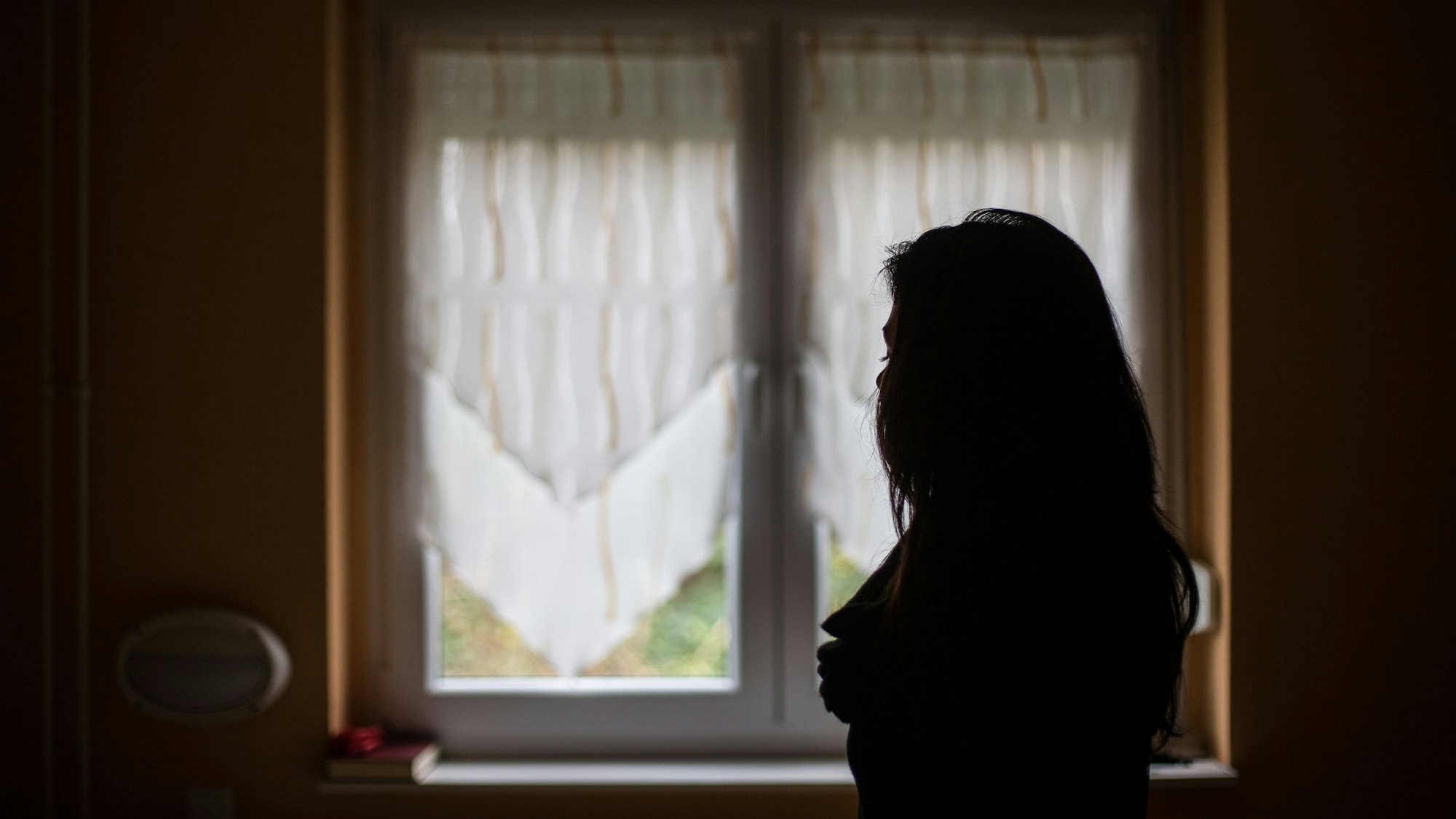 Eine Frau steht an einem Fenster. Zu sehen ist nur ihre dunkle Silhouette.