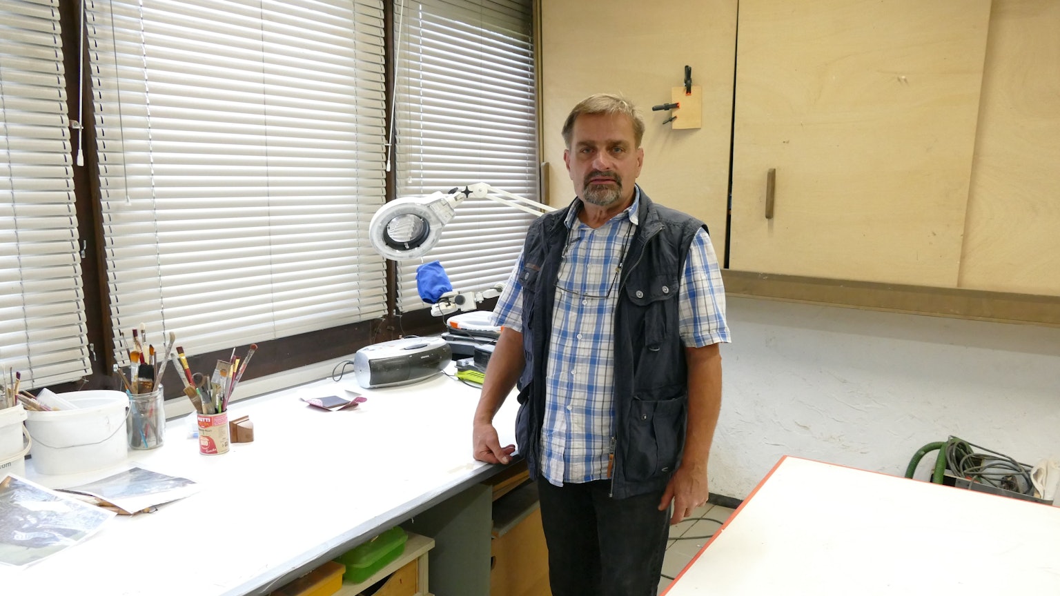 Restaurator Roland Gassert steht an seinem Arbeitsplatz, einem Schreibtisch, in seiner Werkstatt.