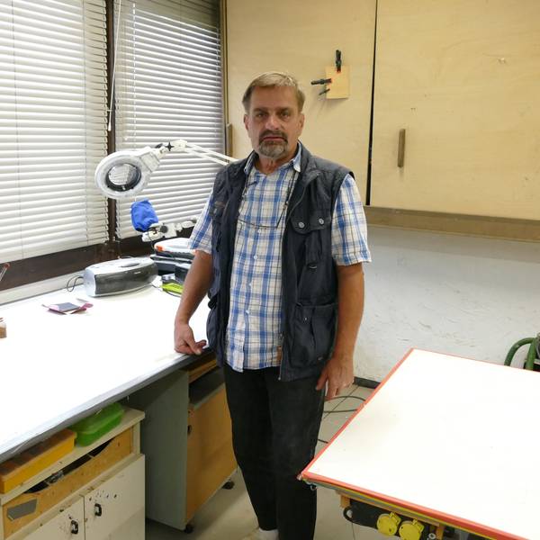 Restaurator Roland Gassert steht an seinem Arbeitsplatz, einem Schreibtisch, in seiner Werkstatt.