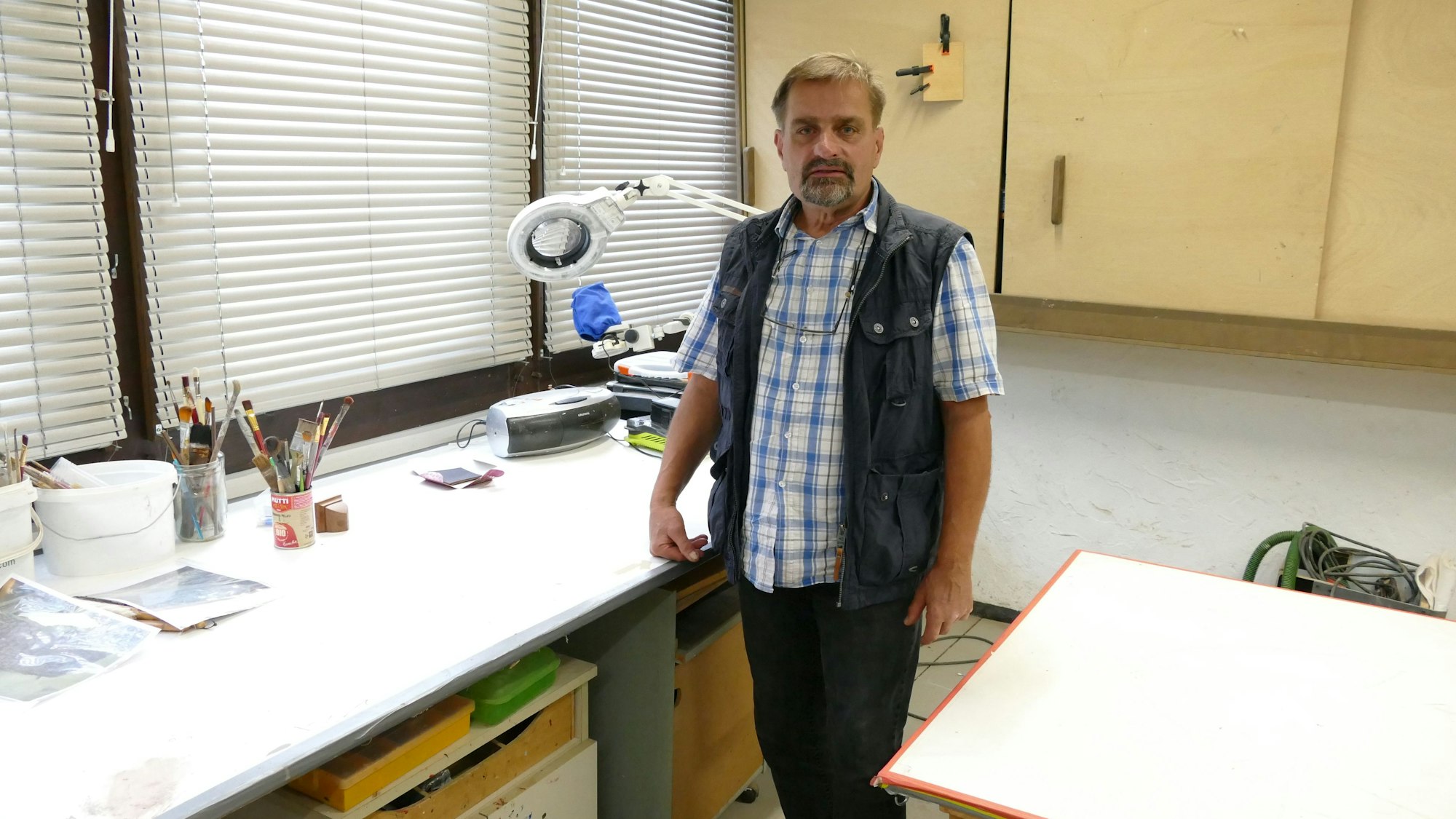 Restaurator Roland Gassert steht an seinem Arbeitsplatz, einem Schreibtisch, in seiner Werkstatt.