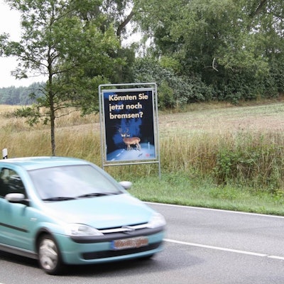 Ein Auto fährt an einem Schild vorbei, das auf Paarungszeit der Rehe hinweist.