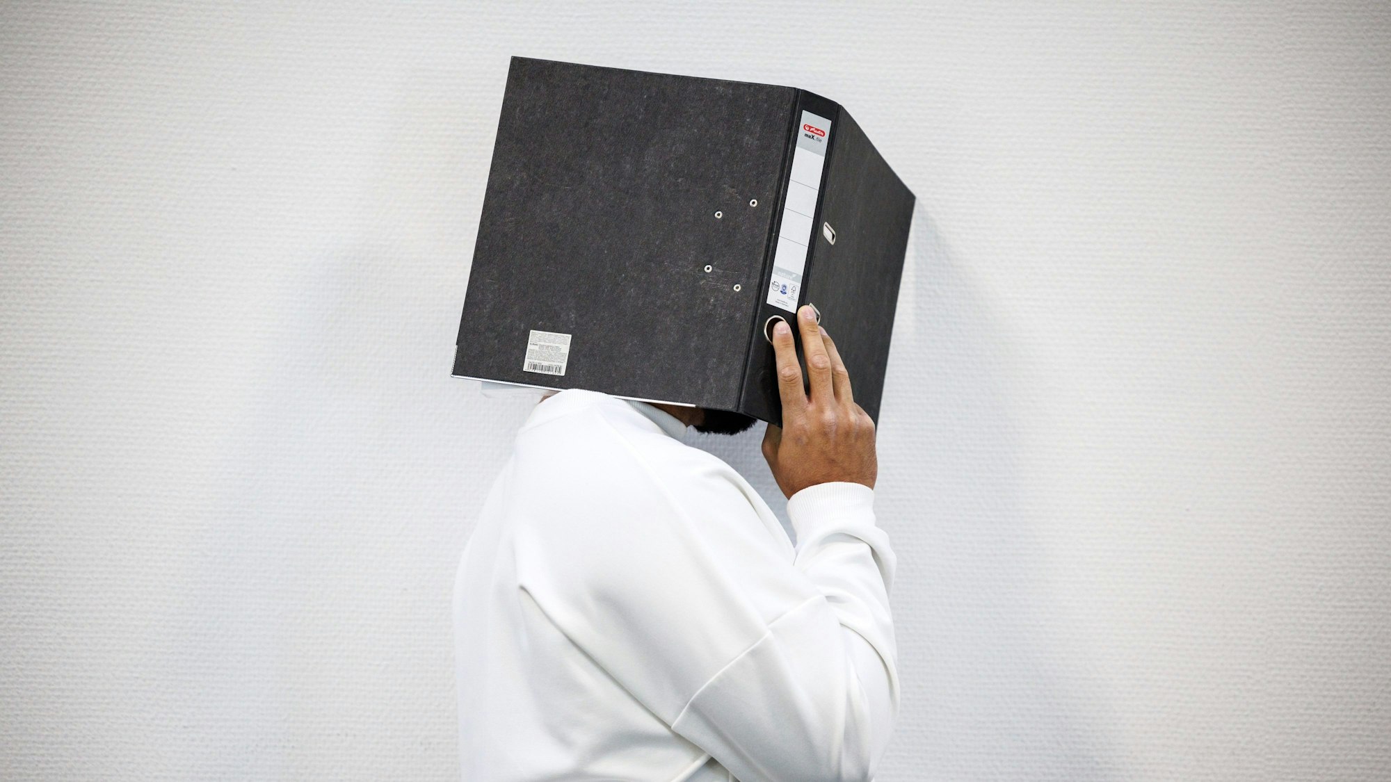 Ein wegen Totschlags angeklagter Mann steht vor Prozessbeginn im Gerichtssaal vom Landgericht und verdeckt sein Gesicht mit einem Aktenordner.