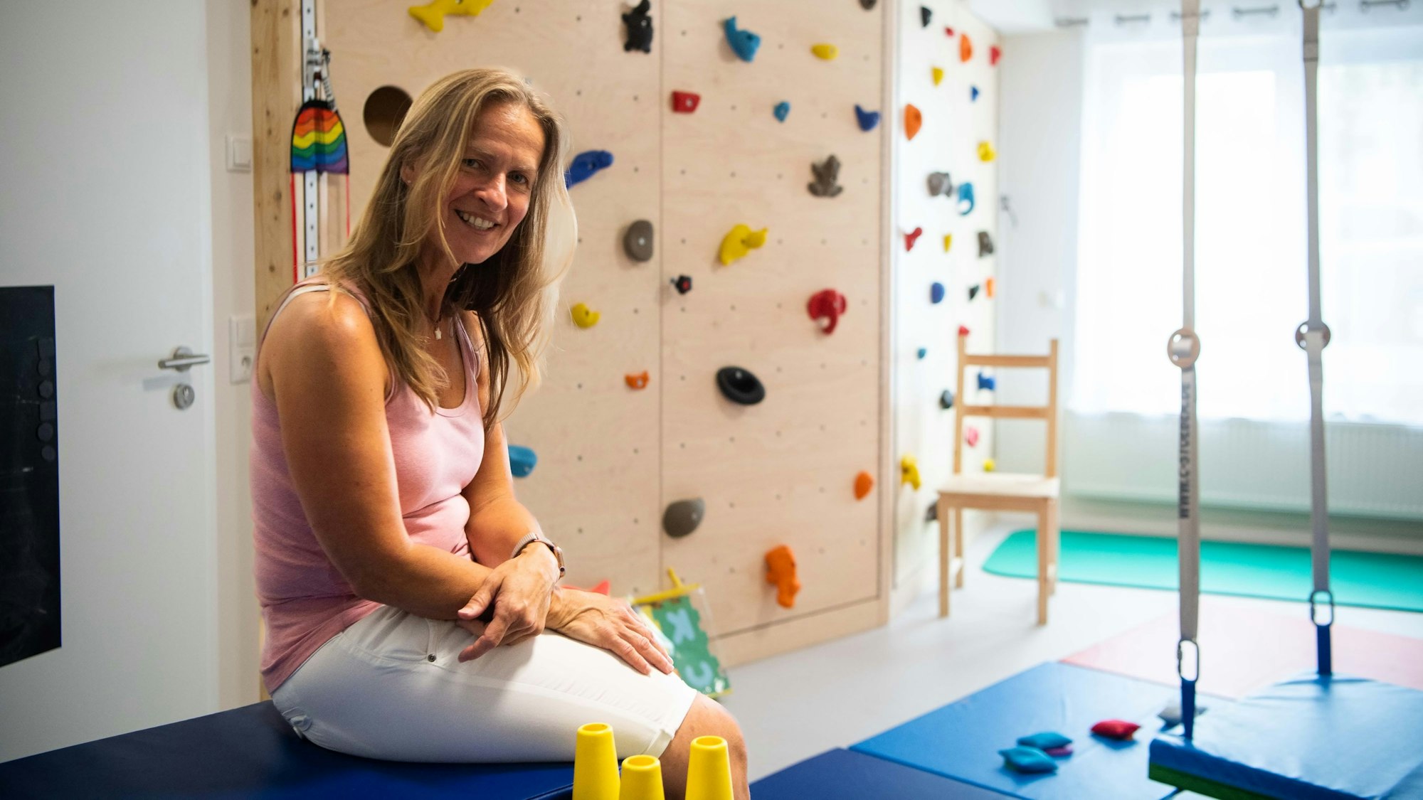 Eine Frau sitzt in einer Ergotherapie-Praxis. Im Hintergrund ist eine Kletterwand zu sehen.
