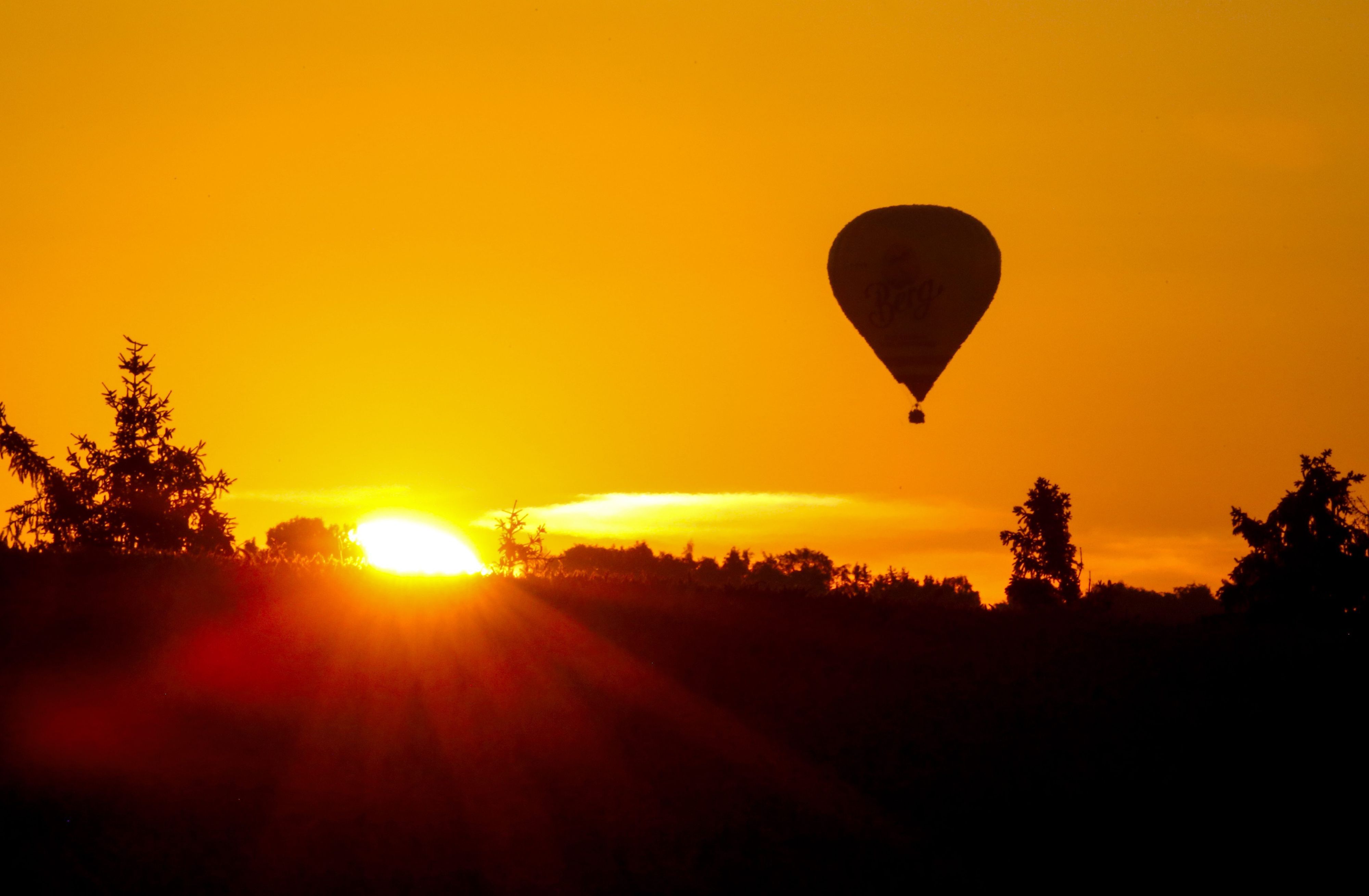dpatopbilder - 15.07.2023, Baden-Württemberg, Munderkingen: Ein Heißluftballon fährt am Himmel, während neben ihm die Sonne auf geht.. Für den heutigen Tag sind Temperaturen über 30 Grad vorhergesagt. Foto: Thomas Warnack/dpa +++ dpa-Bildfunk +++