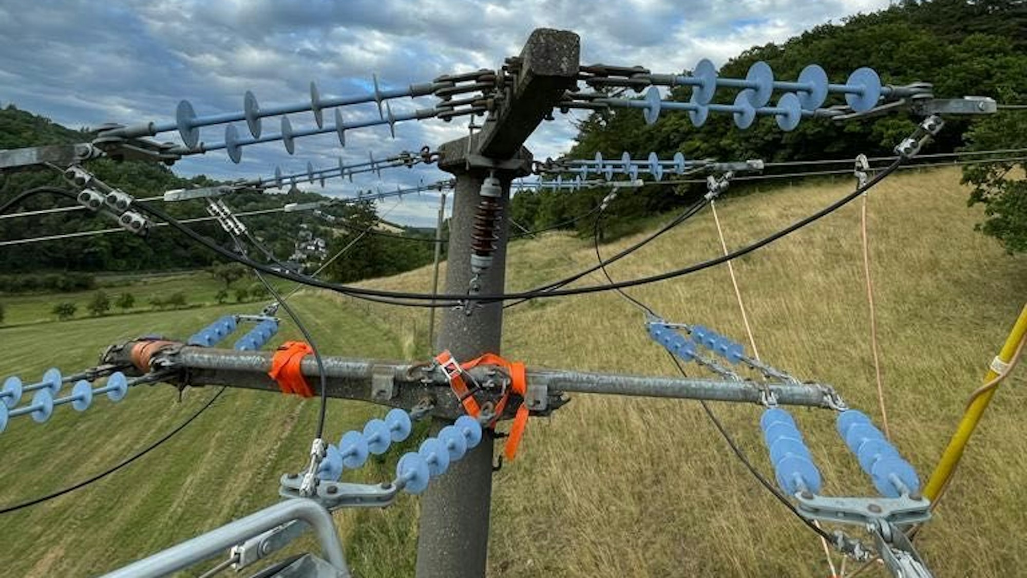 Das Bild zeigt eine mit Spanngurten reparierte Traverse an einer Stromleitung.