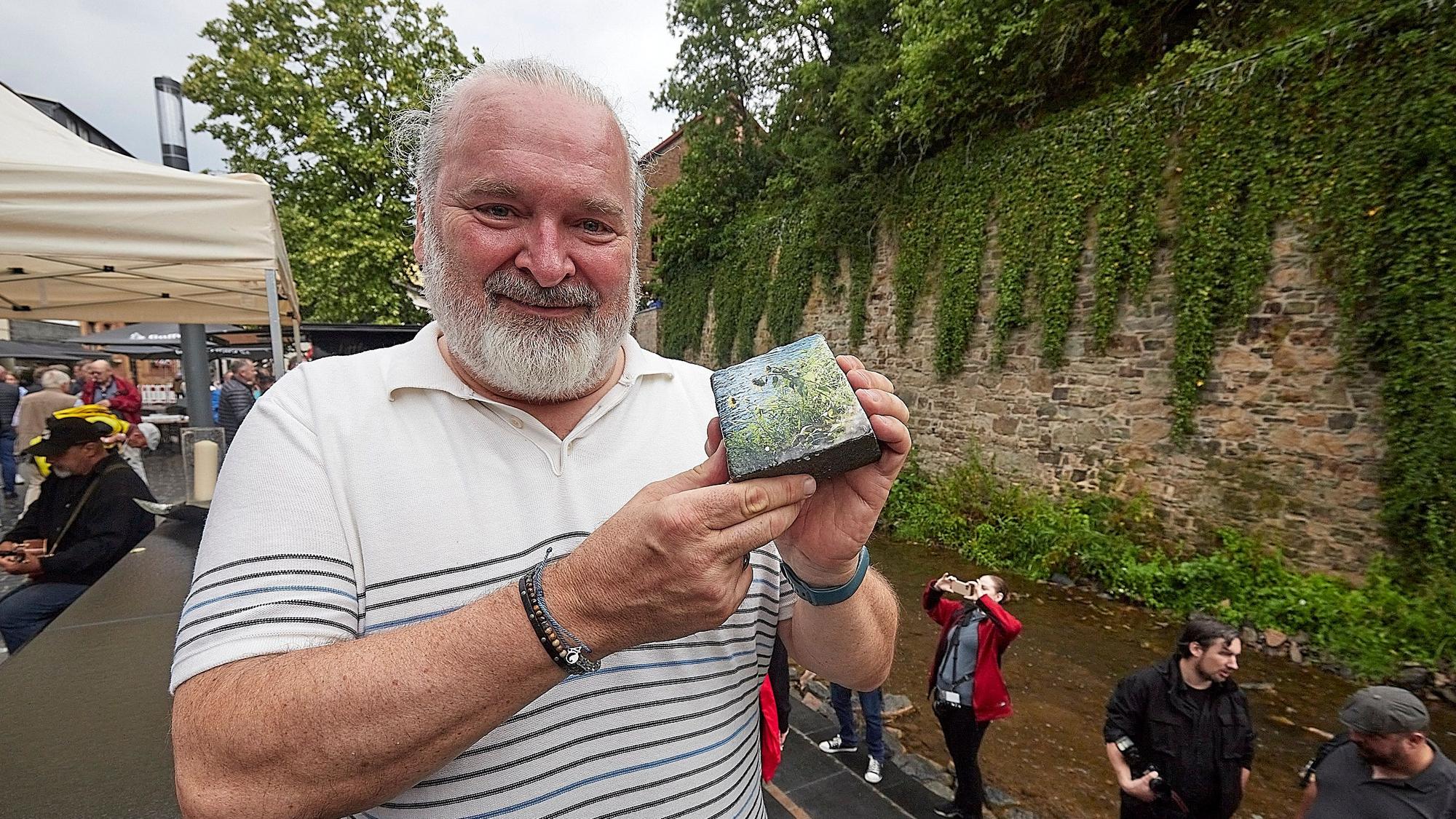 Ein Mann präsentiert einen Pflasterstein, der mit einem Foto bedruckt ist.